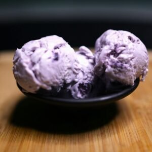 Two scoops of creamy blueberry ice cream in a bowl on a wooden surface.
