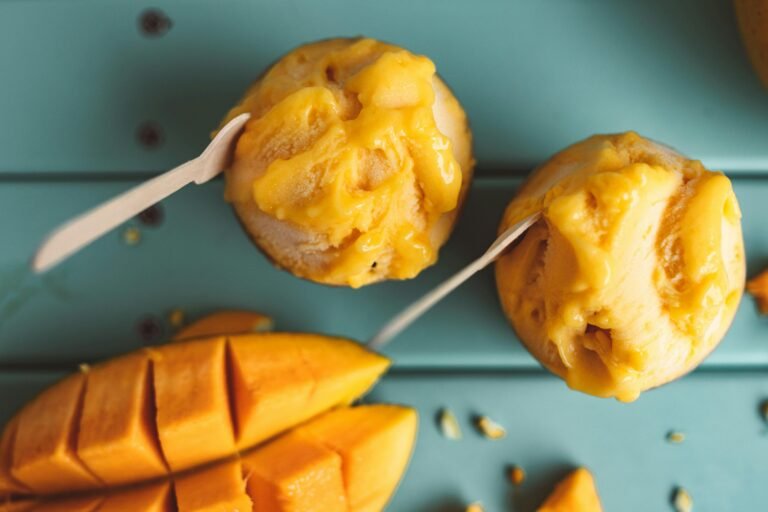 Top view of creamy mango ice cream with fresh mango slices on a teal background.