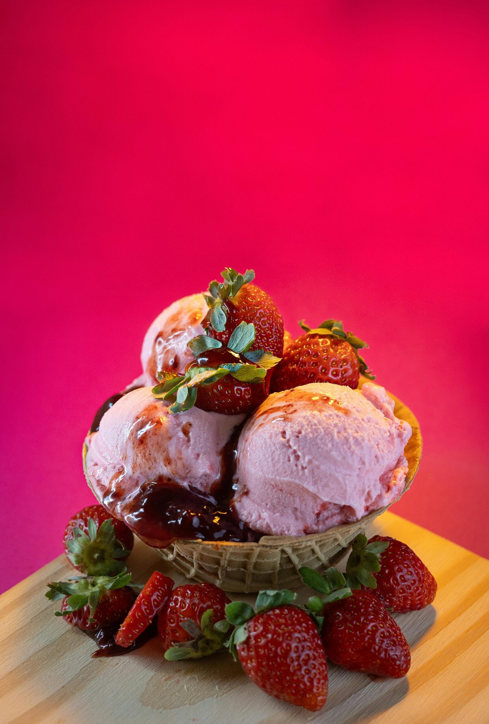 Scoop of strawberry ice cream topped with strawberries in a waffle bowl against a pink background.
