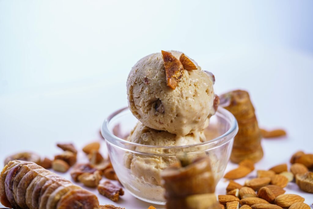 Creamy homemade fig almond ice cream scoops in a glass bowl, surrounded by figs and almonds.