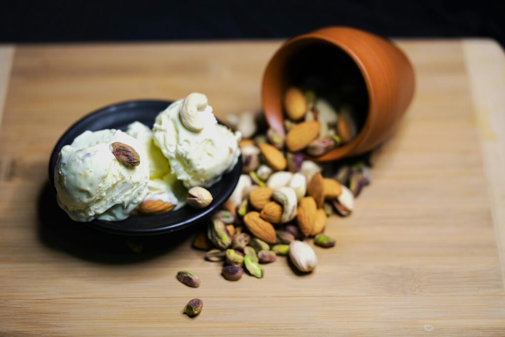 Scoops of ice cream topped with almonds and pistachios, served with mixed nuts on a wooden board.